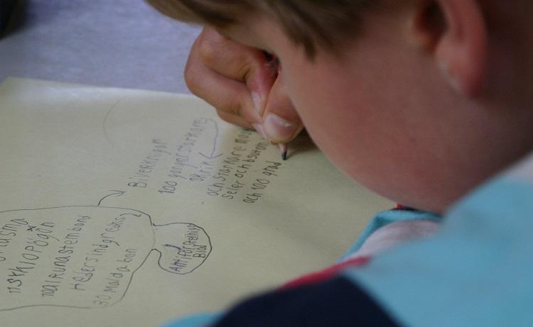 Ett barn som sitter och skriver med penna och papper.