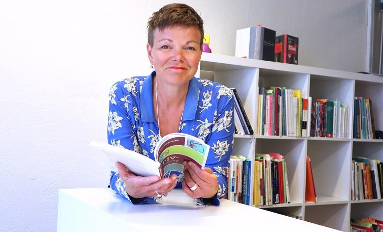 Annette Kronholm-Cederberg sitter vid ett bord och bläddrar i en bok