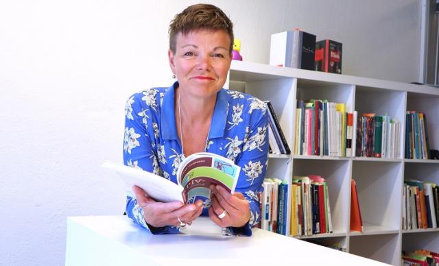 Annette Kronholm-Cederberg sitter vid ett bord och bläddrar i en bok