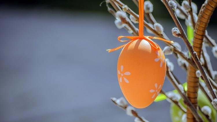 Ett orange påskägg som hänger i påskris med videkissor.