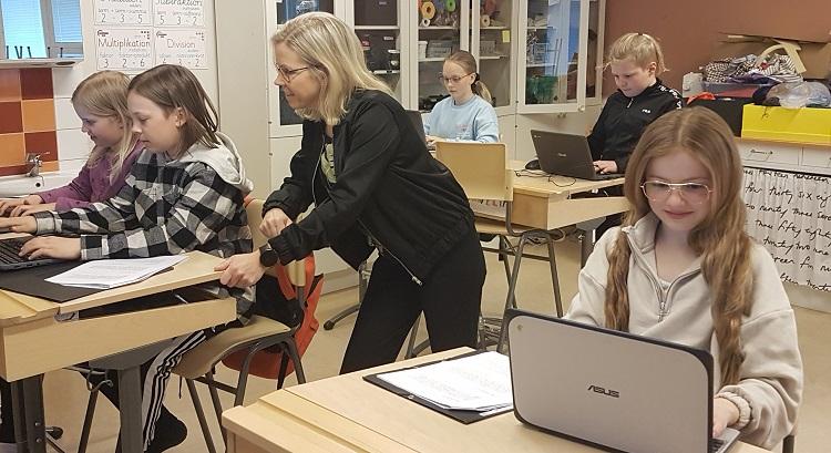 Läraren Maria Boström i klassrummet, där stöttar elever under en skrivlektion. Eleverna sitter vid sina pulpeter och skriver på datorer.